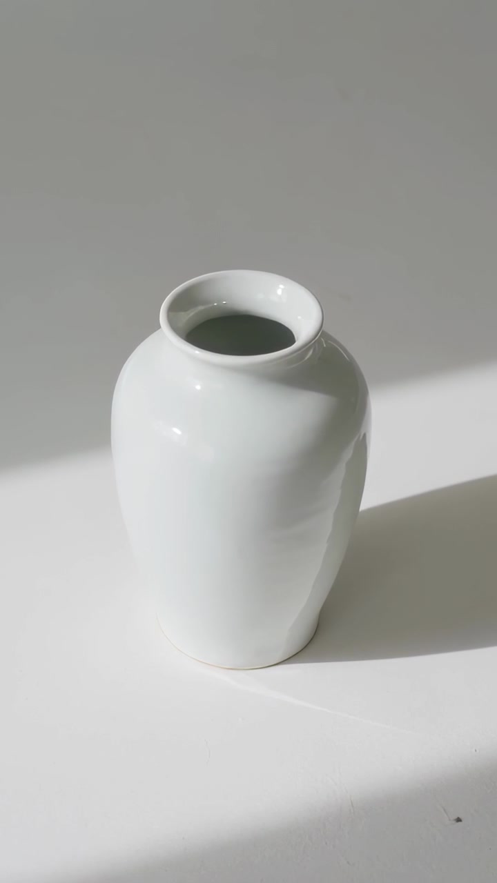 Video verticale: Sole in movimento proietta un'ombra obliqua sul tavolo, spostando un vaso smaltato che luccica e un riflesso.