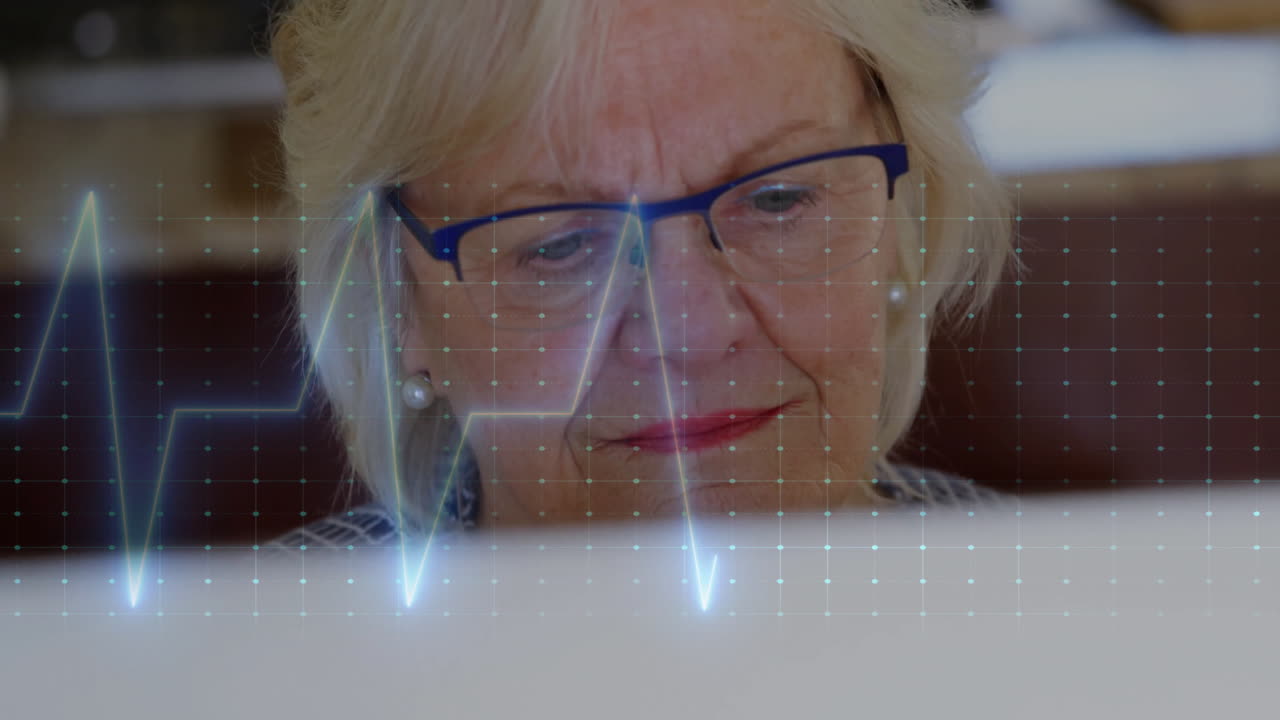 Animation of cardiograph over senior caucasian woman using laptop