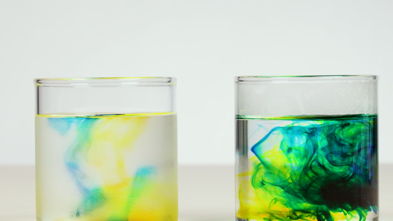Colored dye disperses in two glasses of water, demonstrating diffusion rates under bright, even lighting