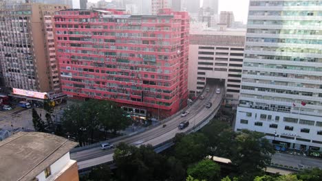 Traffic-passing-through-a-Car-park-building-in-downtown-Hong-Kong,-with-city-mega-buildings,-Aerial-view