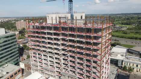 Drone-pullback-from-rusted-iron-bars-on-newly-constructed-apartment-offices-and-large-crane-in-suburb-city