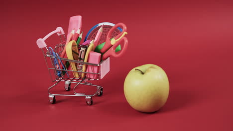 cerrar el carrito de compras con artículos escolares y manzana sobre fondo rojo