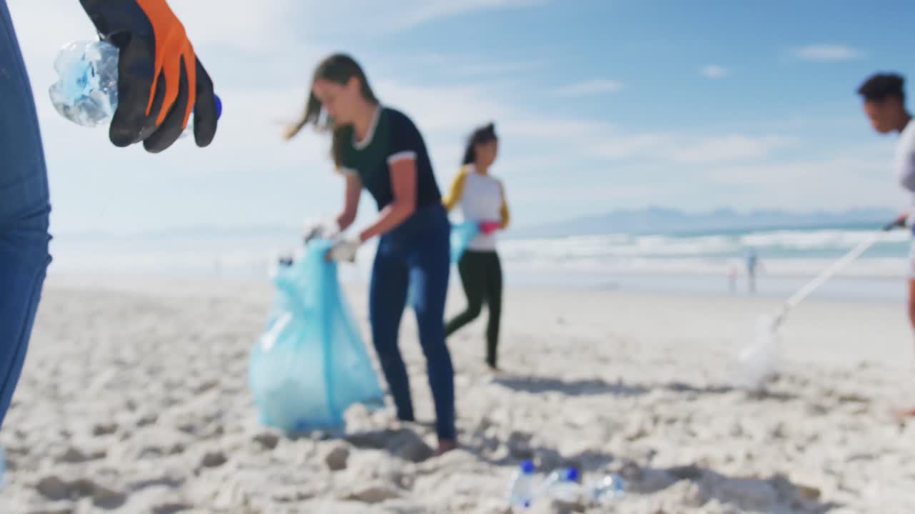 다양한 여성 친구 들 이 해변 에서 쓰레기 가방 에 쓰레기 를 넣고 있다