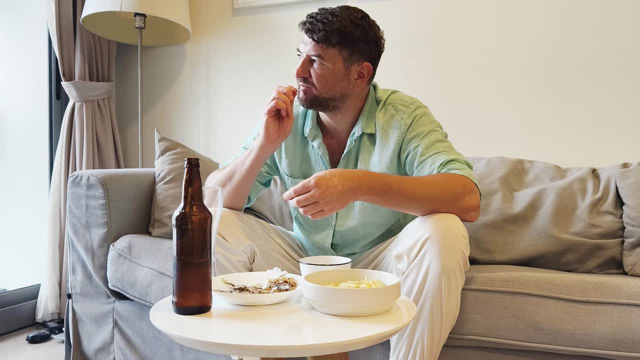 Man Pouring Beer and Eating Snacks on Sofa at Home