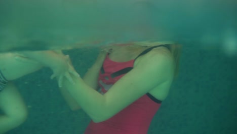 side view, an underwater shot of young woman in pink swimming suit supporting his son in water pool. teaching how to swim. indoors swimming pool