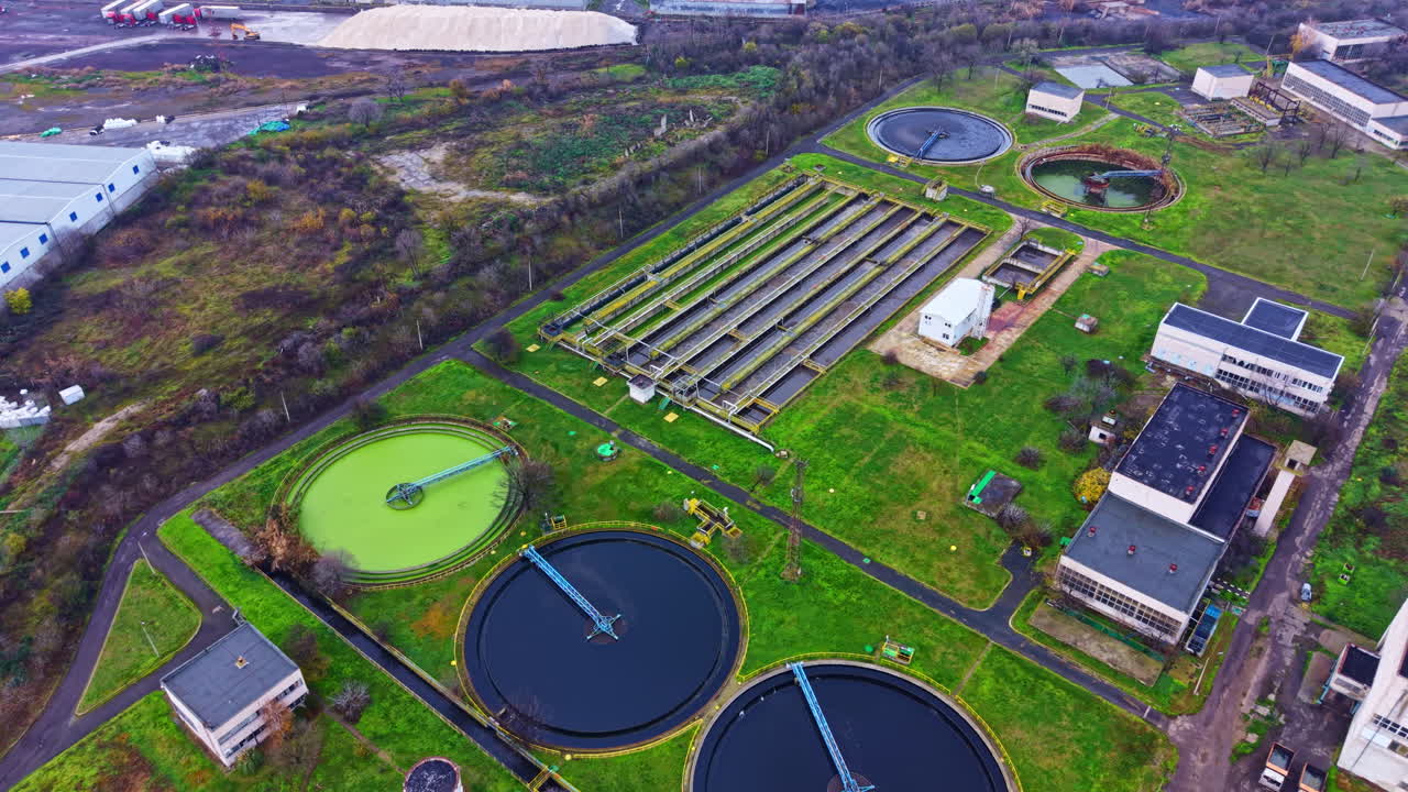 View of a water treatment facility with large tanks and green areas in an industrial area near a city at midday
