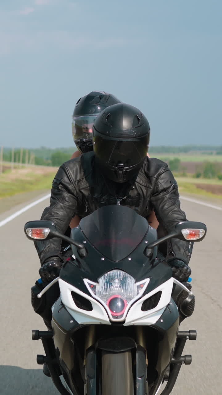 Couple with hardhats travels by contemporary motorcycle together along highway between empty plowed fields on sunny spring day slow motion