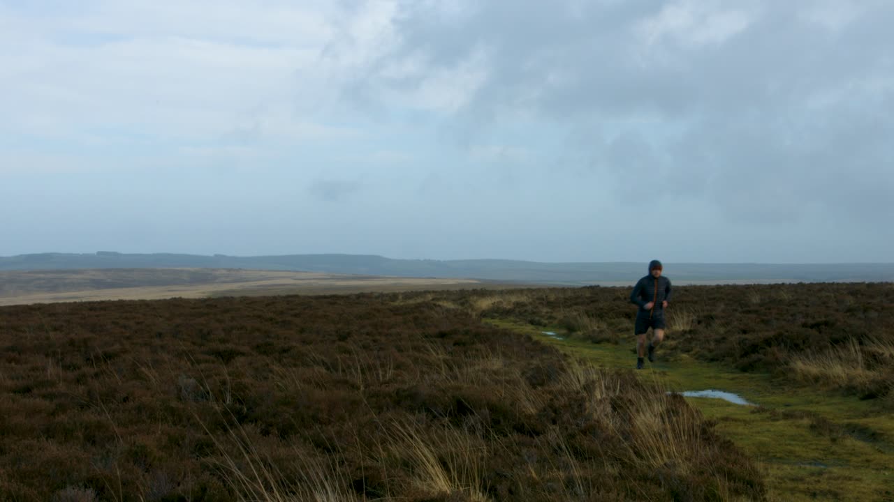 corredor masculino entrenando en exmoor corriendo frente a la cámara con fondo de campo rural reino unido 4k