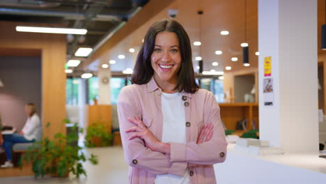 portrait of businesswoman standing in busy open plan office with colleagues in background