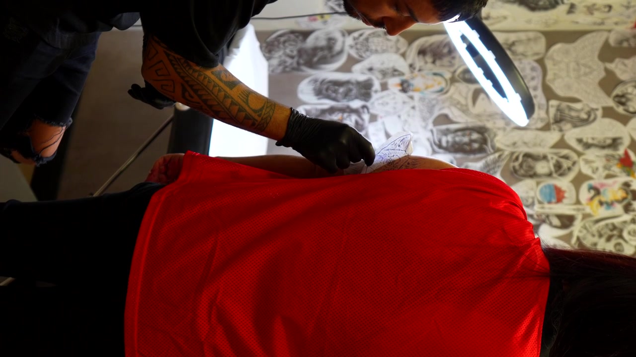 Tatuatore che rimuove la carta con la traccia del tatuaggio dal braccio della sua cliente. Ripresa verticale a mano libera