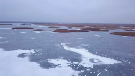 冬天的冰<unk>湖liepaja的空中景色, 破裂的藍色冰, 乾燥的黃色<unk>島, 陰<unk>的冬天, 寬<unk>無人機拍攝向前移動的攝影機向下傾斜