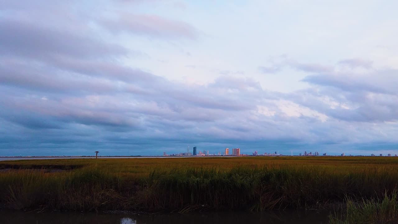 hd motionlapse zoom de izquierda a centro horizonte de la ciudad atlántica en la distancia sobre la vía fluvial con cielo mayormente nublado de día a noche con nubes que se vuelven rosas, moradas y azules