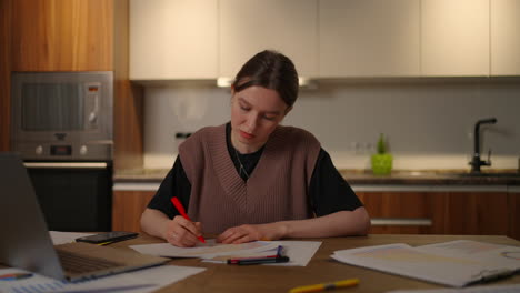 A-pensive-woman-looks-at-the-documents-and-the-graphs-on-the-table-make-notes-in-the-papers.-A-tired-woman-works-from-home.-Distance-Learning-Analysis-and-Planning