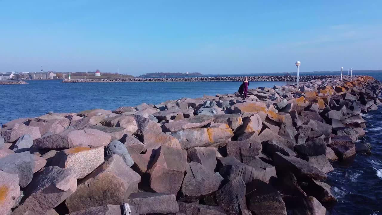 해안선 근처의 바위에 서 있는 공중 젊은 여성