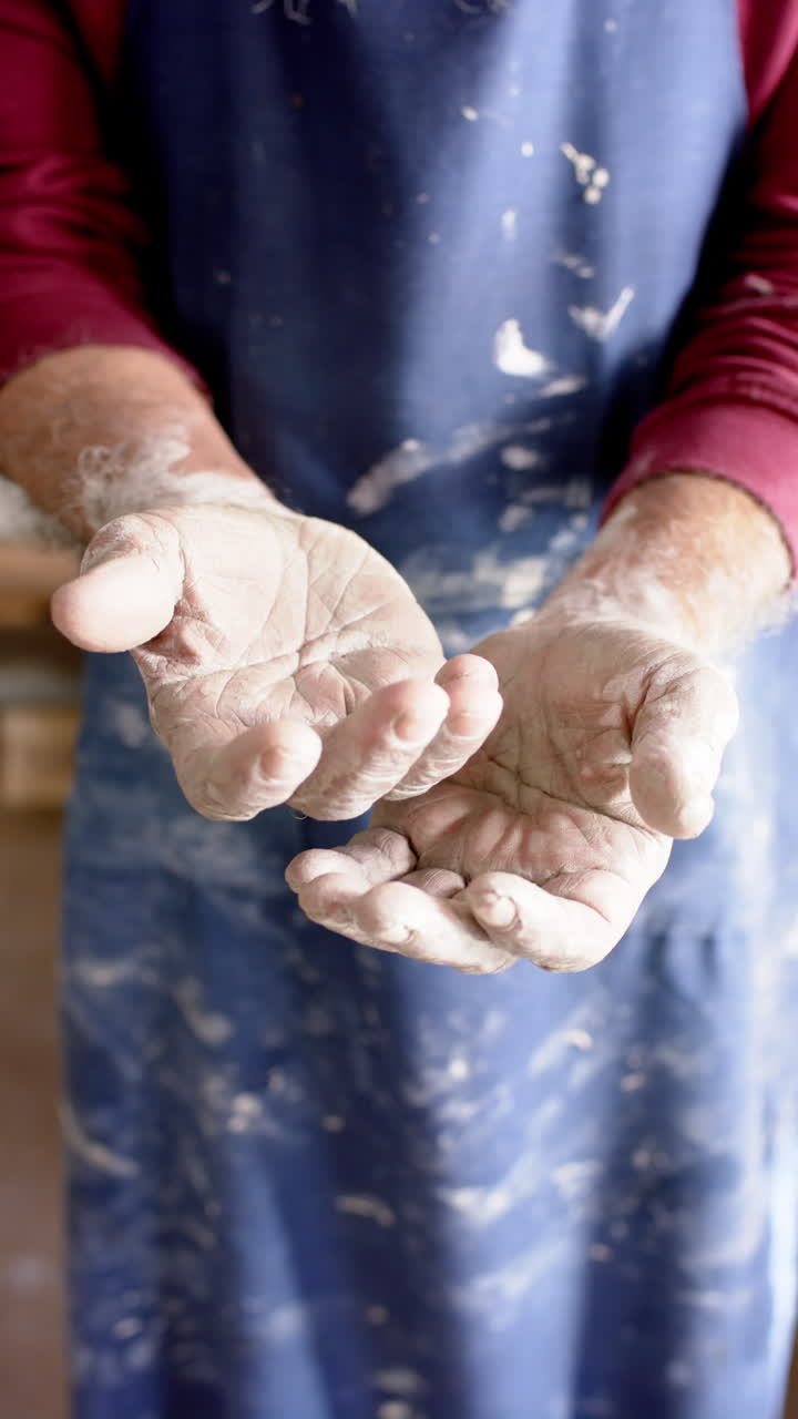 Dirty hands of biracial male potter with long beard, standing in pottery studio, slow motion