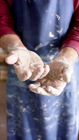dirty hands of biracial male potter with long beard, standing in pottery studio, slow motion