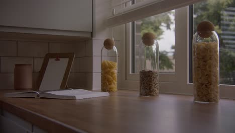 kitchen work surface with a cookbook open on it and jars of pasta