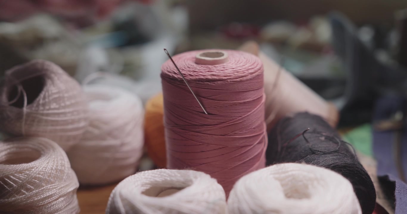 Gros plan sur une aiguille à coudre insérée dans une bobine de fil de coton rose entourée de fils colorés, mettant en valeur la couture et l'artisanat textile.