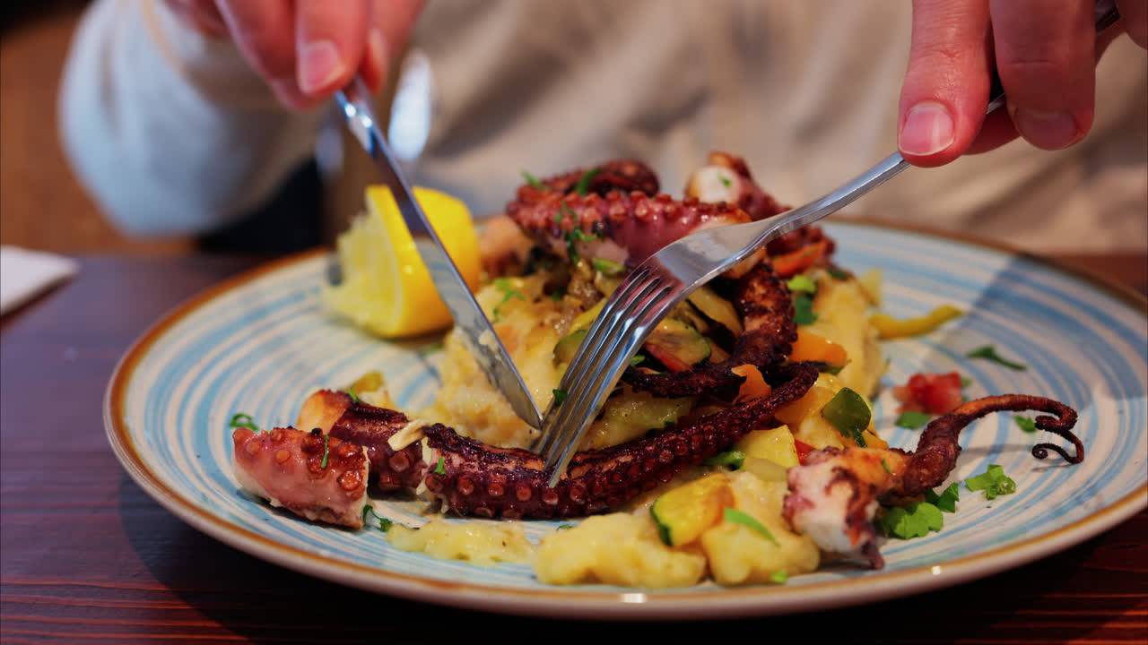 Close up of a man cutting and eating grilled octopus on a puree at a restaurant