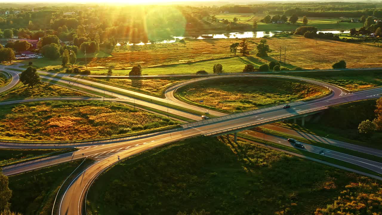 Vehicles Driving Through Cloverleaf Intersection at Sunset Golden Sunlight in Latvian Countryside
