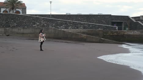 young asian female standing on the sand and takes a picture of the waves