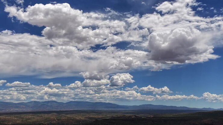 Timelapse 4K con dron de un clima cambiante del suroeste y nubes estratificadas. Un sistema meteorológico se desplaza por un cielo brillante, proyectando sombras sobre un vasto paisaje de desierto alto y una cordillera distante.