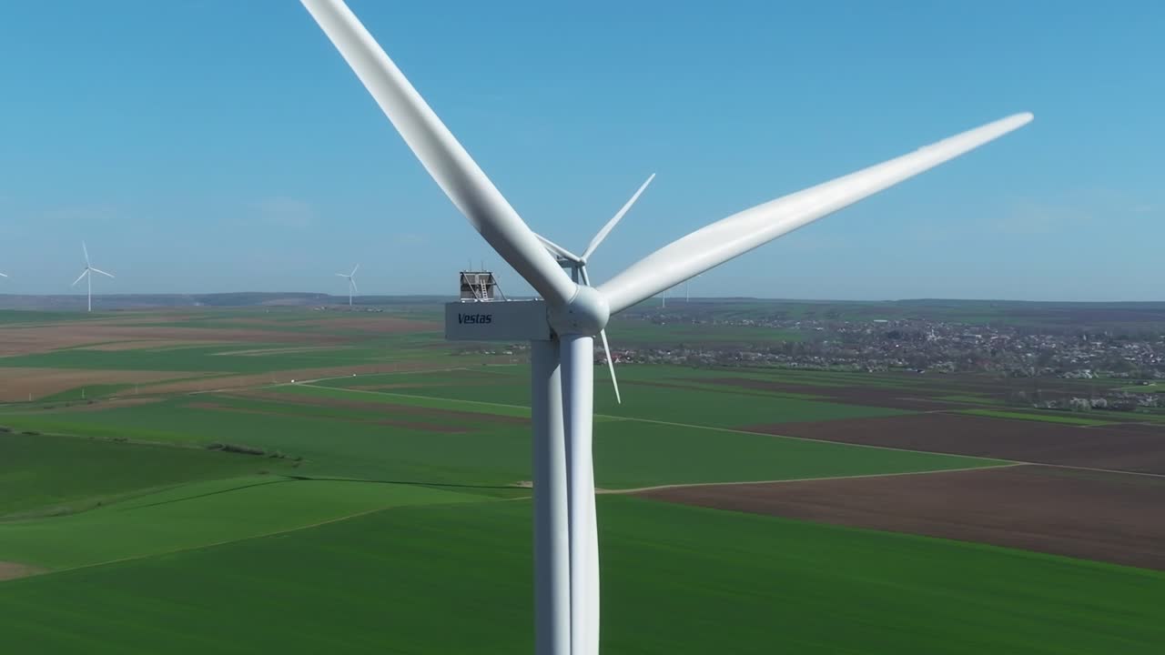 풍력 터빈은 광활한 녹색 과 먼 마을에서 이 나는 빛 날에 회전합니다.