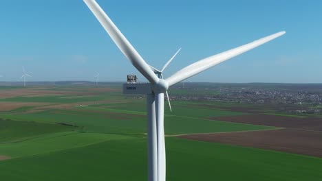 Wind-turbines-spinning-on-a-sunny-day-over-vast-green-fields-and-distant-village