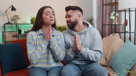 Young-family-marriage-couple-praying-sincerely-with-folded-arms-asking-God-for-help,-begging-apology