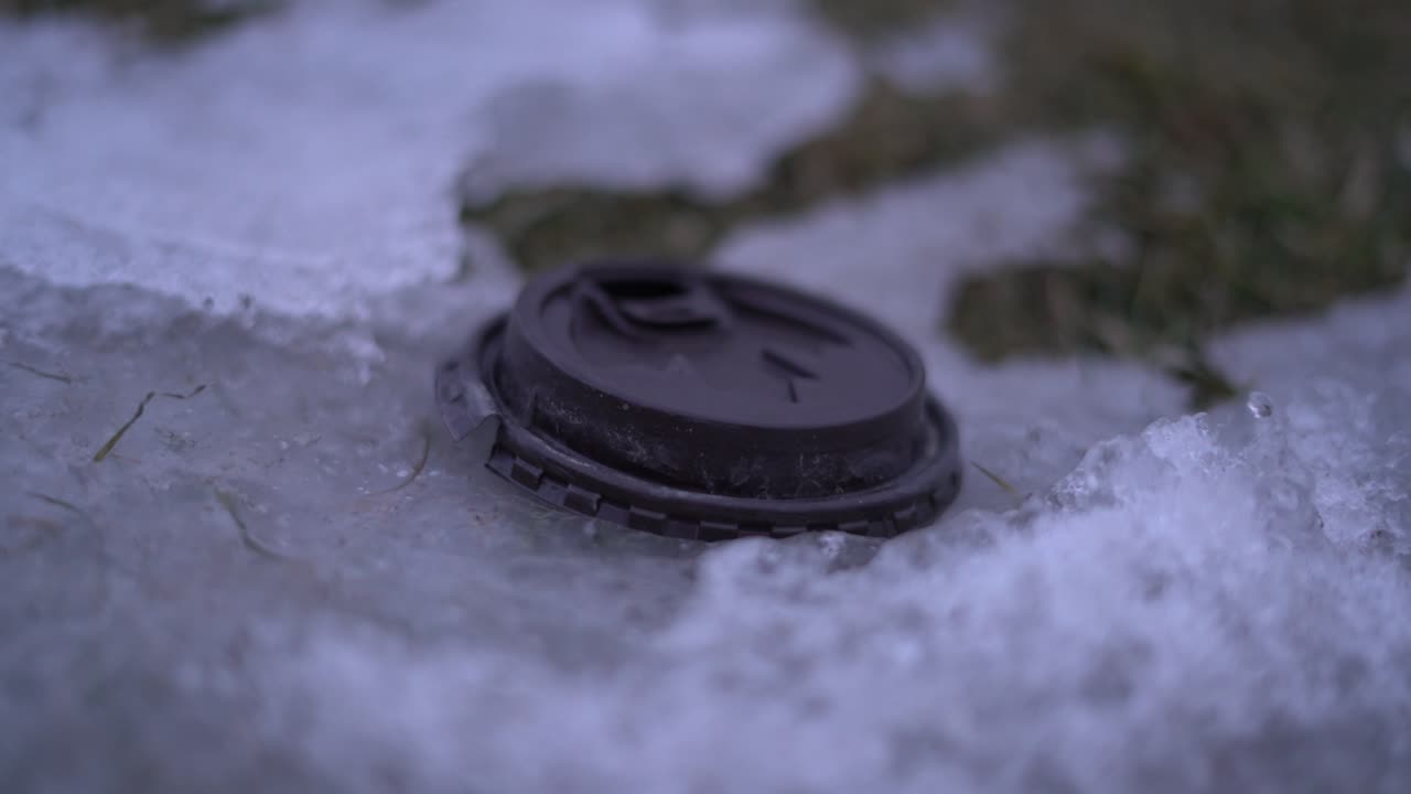 Śmieci w Kanadzie z kubkiem po kawie z Tim Hortons leżącym na ziemi zimą na poboczu drogi otoczonym śniegiem - plastikowa nakrętka z kubka po kawie wyrzucona na pobocze drogi na zewnątrz.