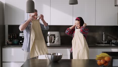 pareja alegre cocinando juntos en casa en la cocina, poniendo delantales