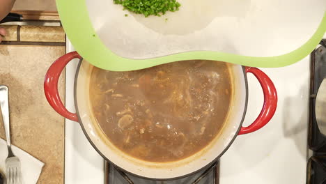 adding chopped chives and minced garlic to wild rice mushroom soup simmering on the stove top - overhead view wild rice series