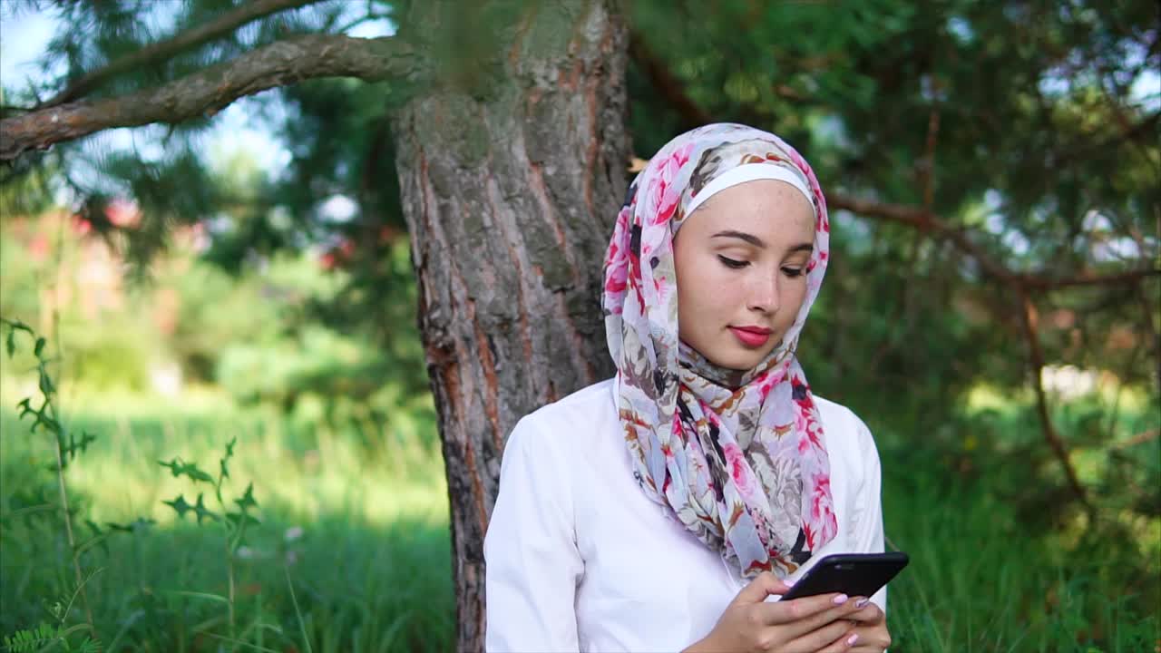 Woman using phone in park wearing hijab