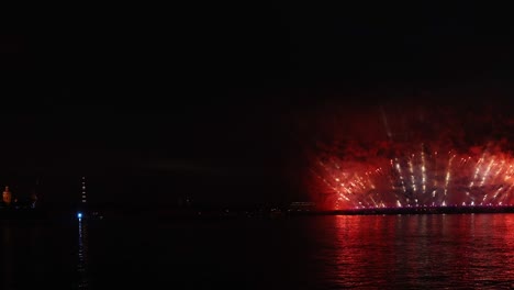 fuegos artificiales coloridos festivos e iluminación en el cielo oscuro con un hermoso reflejo en el agua. velas escarlata de vacaciones