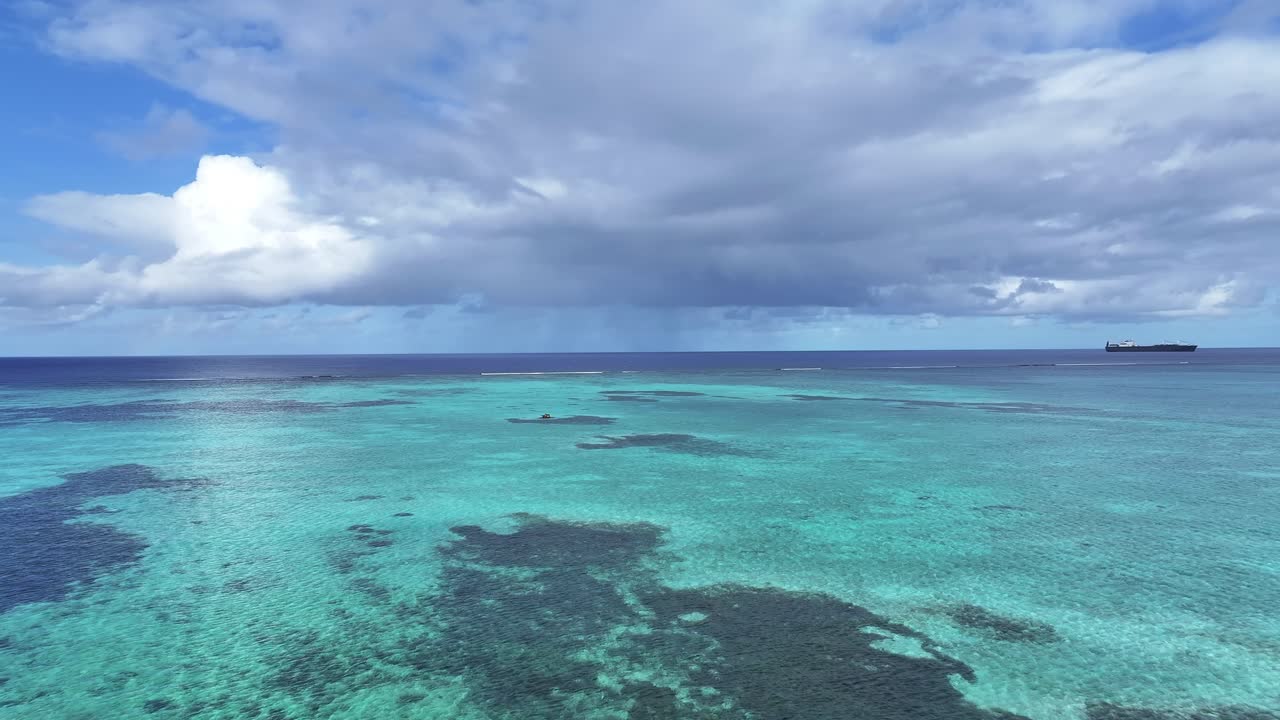 "A stunning aerial drone shot capturing the calm and crystal-clear emerald waters of Saipan’s west coast. Features beautiful coral reefs visible through the transparent sea."