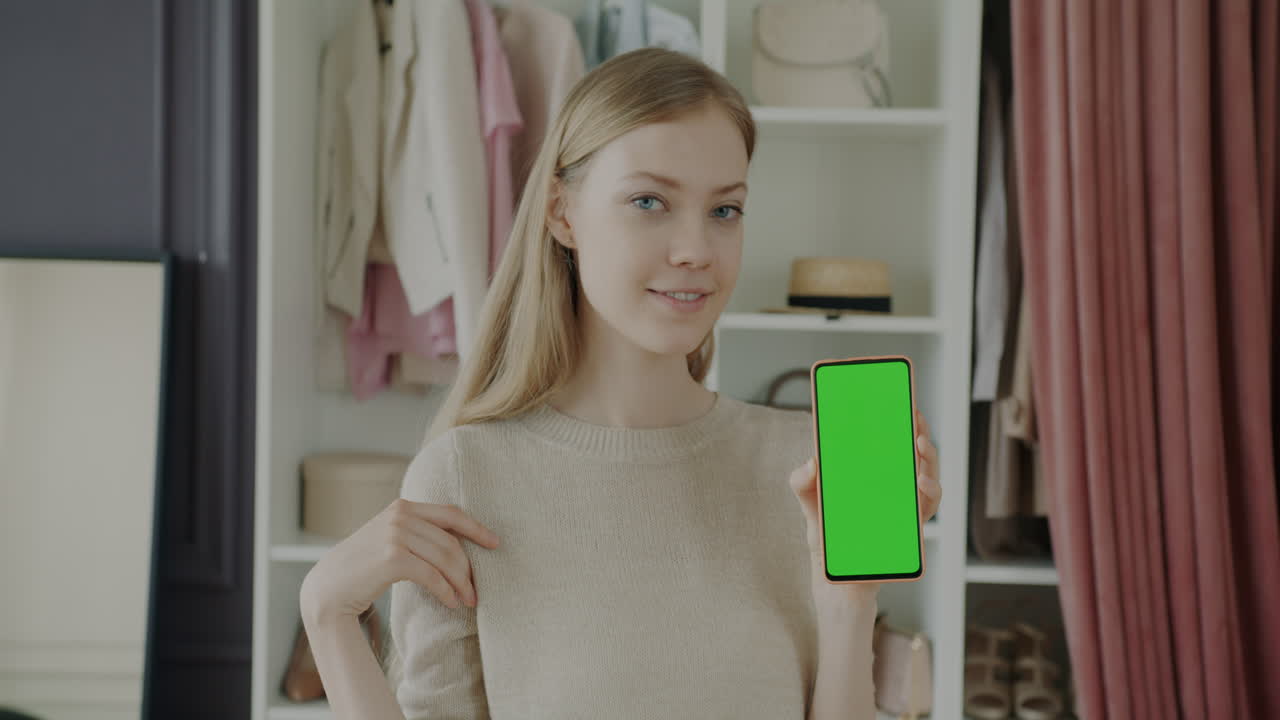 Woman holding a phone with a green screen in a clothing store