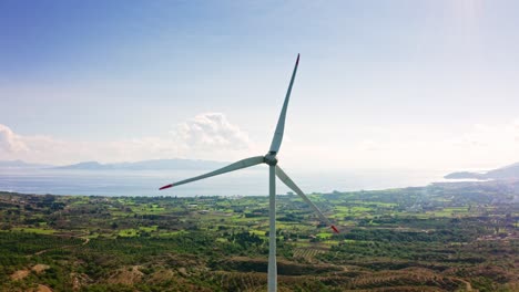 Vanes-of-wind-power-generator-rotating-on-the-background-of-Turkish-sunny-rural-landscape-and-Aegean-sea,-Kızlan-village,-Reşadiye-peninsula