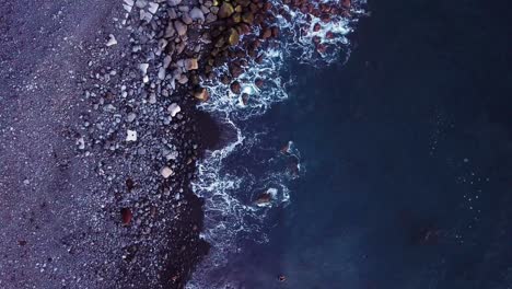 aerial topdown shot of rocky coast with little pier and waves crushing the coast, paul do mar, madeira, portugal