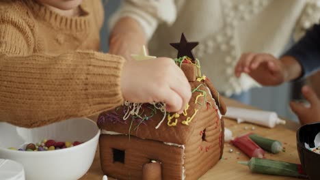 tilt down video of family decorating together gingerbread house