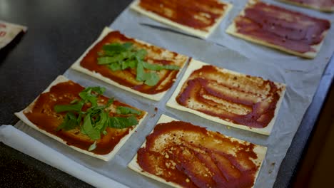 preparación cercana de pizza de pan plano con hojas de albahaca colocadas