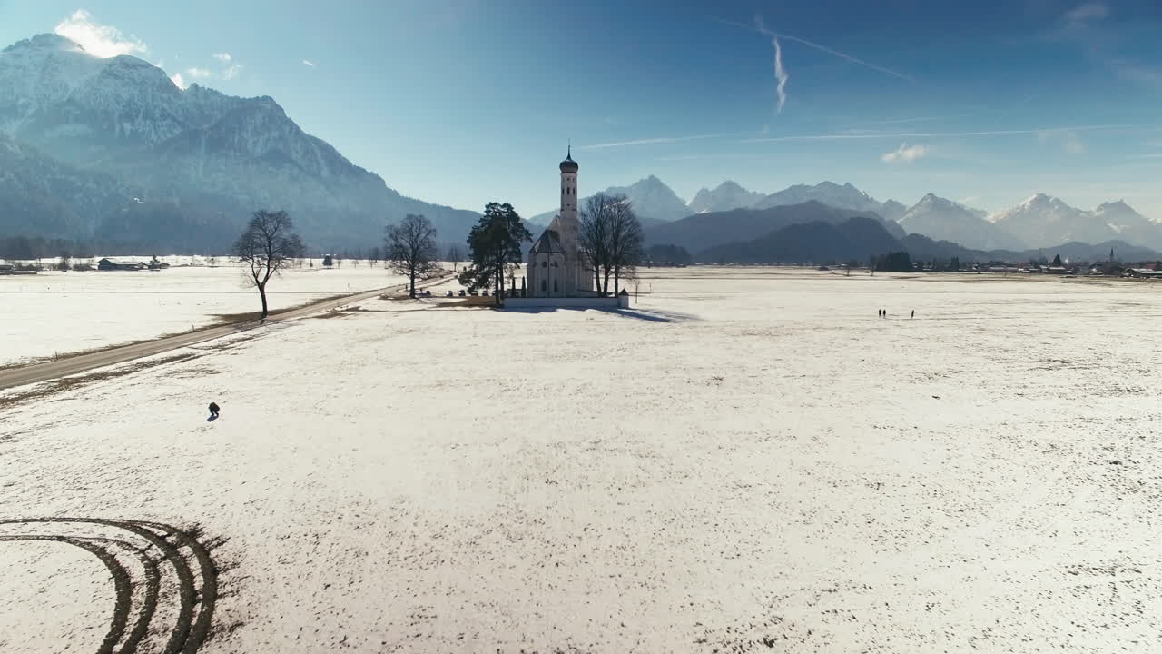 Aerial clip of a Church in the middle of big fields, with mountains in the background, during winter