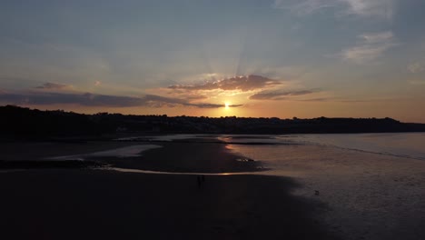 Sunset-rays-beam-fiery-golden-colours-across-relaxing-beach-ocean-coastline-aerial-view-low-slow-left-dolly