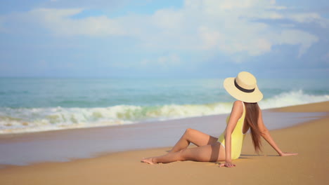 Mujer-Solitaria-En-Traje-De-Baño-Y-Sombrero-De-Verano-Sentada-En-La-Arena-De-La-Playa,-Mirando-Las-Olas-Del-Mar-Tropical-En-Un-Día-Soleado,-Cámara-Lenta