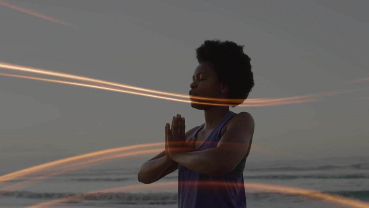 Donna che alza e abbassa le braccia in posizione di meditazione al petto sulla riva, con strisce di luce che la avvolgono