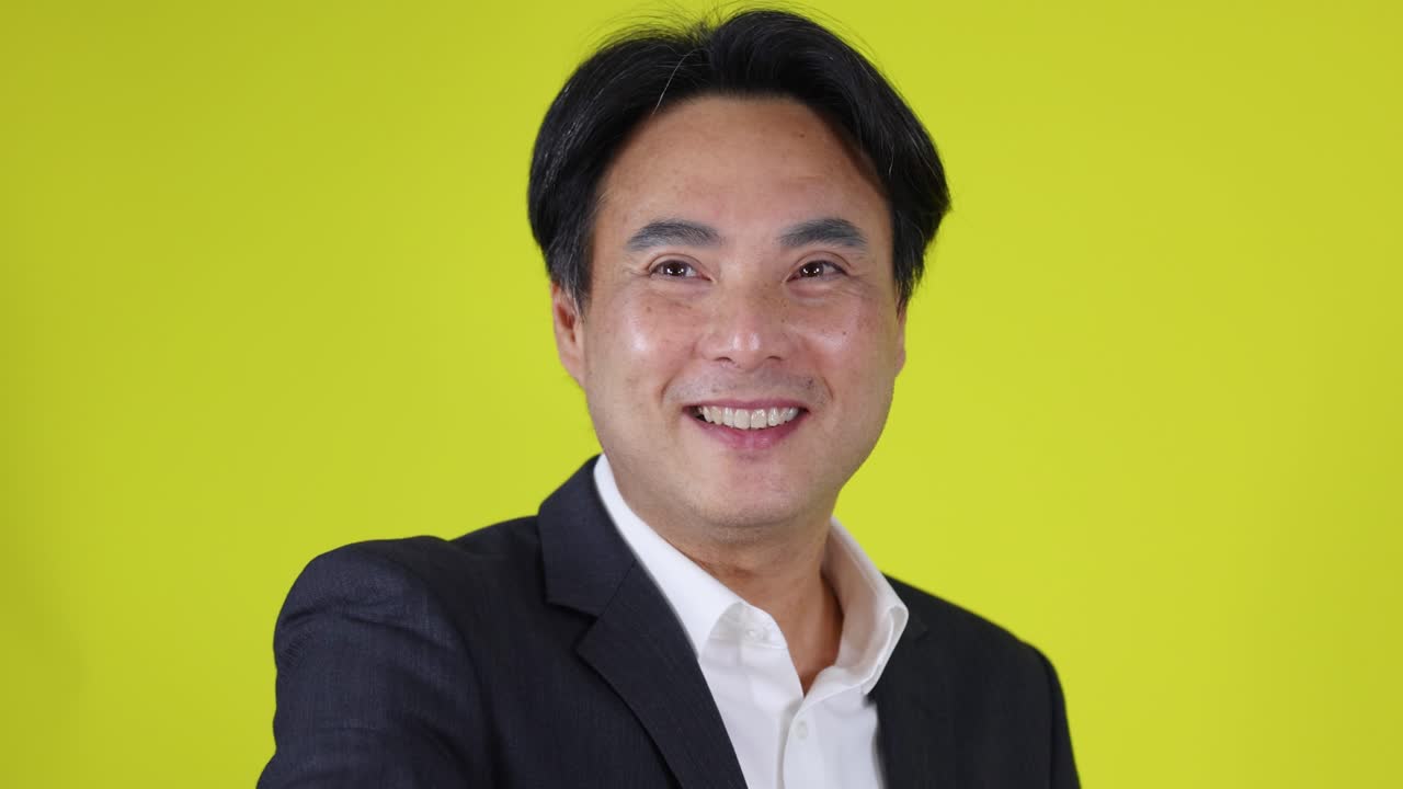鮮やかな黄色の背景に、明るい照明の下、笑顔で歓迎のジェスチャーをするスーツ姿の自信に満ちたビジネスマン