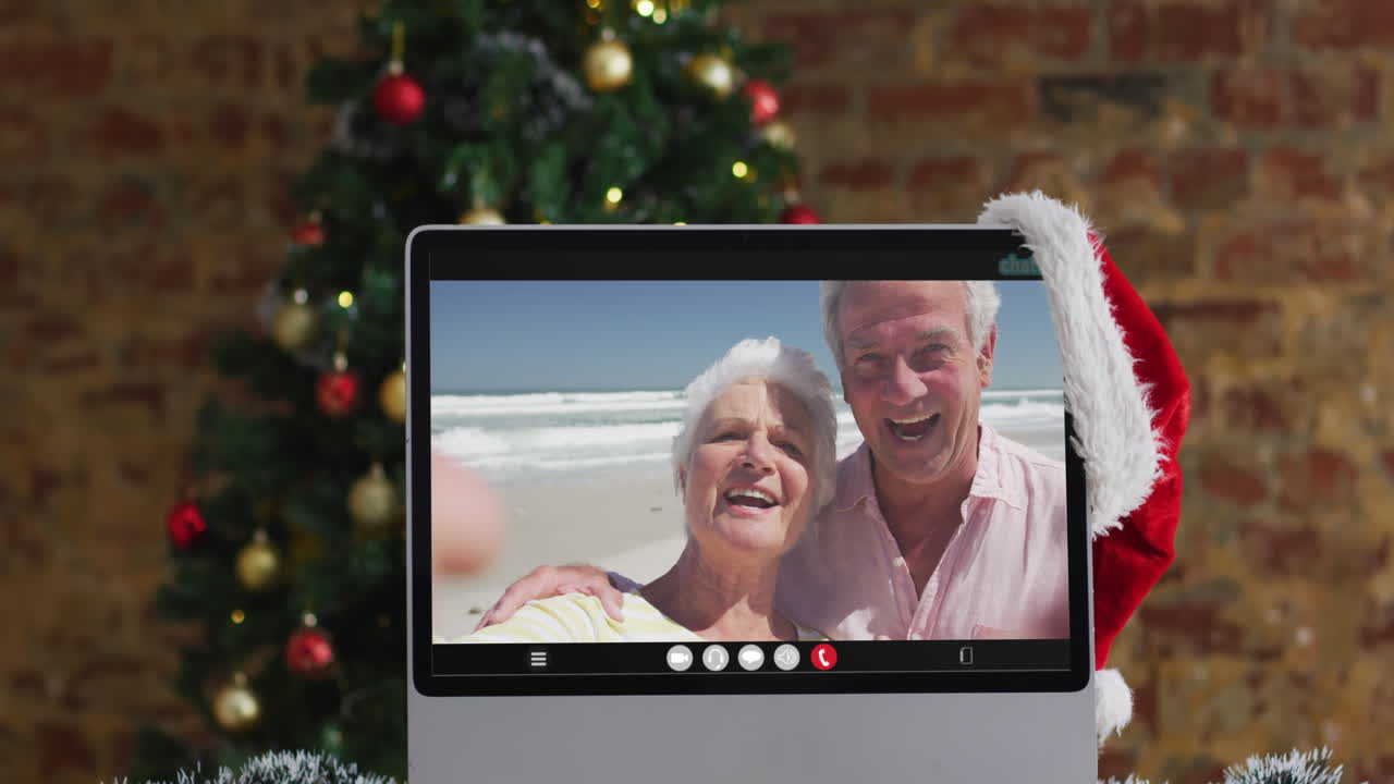 una pareja de alto nivel caucásica saludando en una videollamada en la computadora, con un árbol de navidad