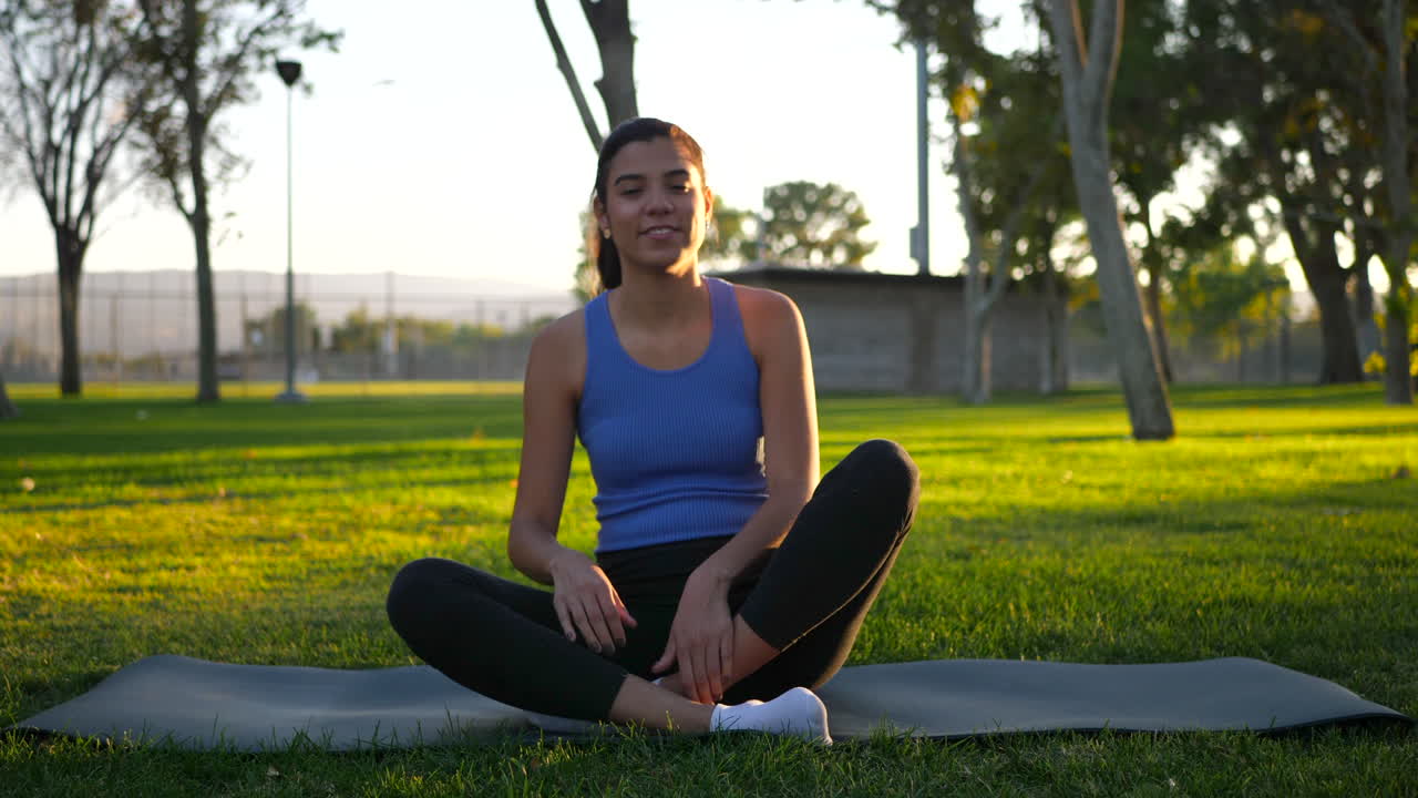 colocar a una joven hispana yogui saliendo de la posición de loto en su alfombra de yoga después de una meditación pacífica durante el amanecer en un parque de césped