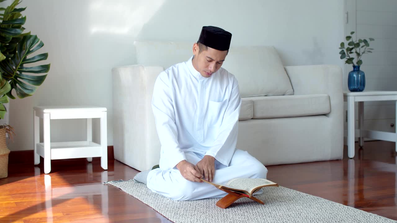 이슬람 의복 을 입은 젊은 이슬람 남자 가 꾸란 을 읽고 있다