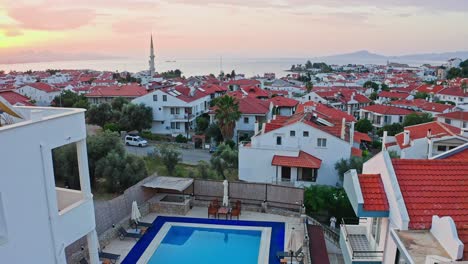 Drone-flight-above-houses,-courtyards-and-swimming-pool-of-small-seaside-town-at-romantic-morning-dawn,-Mediterranean-Turkey,-Muğla-province