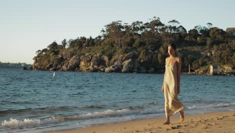 Joven-Hispana-Camina-Por-La-Playa-Con-Vestido-Largo-Durante-Una-Hermosa-Puesta-De-Sol